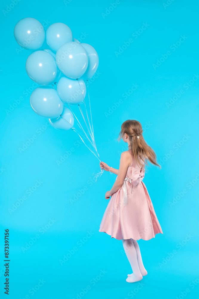 Young Girl in Pink Dress Holding Blue Balloons Against Blue Background Young Girl in Pink Dress Holding Blue Balloons Against Blue Background