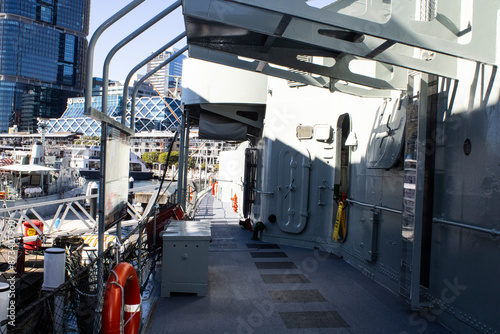 A stunning daylight shot capturing the intricate details of a ship's metallic deck, set against the backdrop of majestic Australian naval warships and beautiful architectural structures.