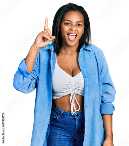 Beautiful hispanic woman wearing casual denim jacket pointing finger up with successful idea. exited and happy. number one.