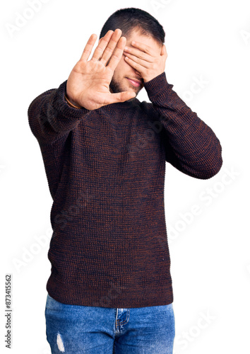 Young handsome man wearing casual sweater covering eyes with hands and doing stop gesture with sad and fear expression. embarrassed and negative concept.