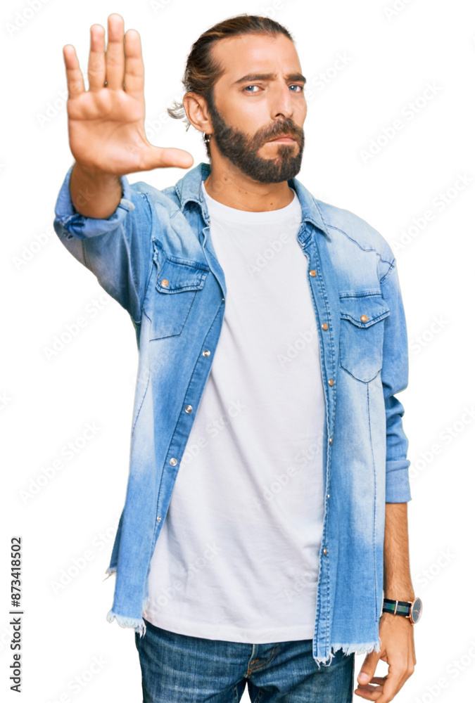 Attractive man with long hair and beard wearing casual denim jacket doing stop sing with palm of the hand. warning expression with negative and serious gesture on the face.