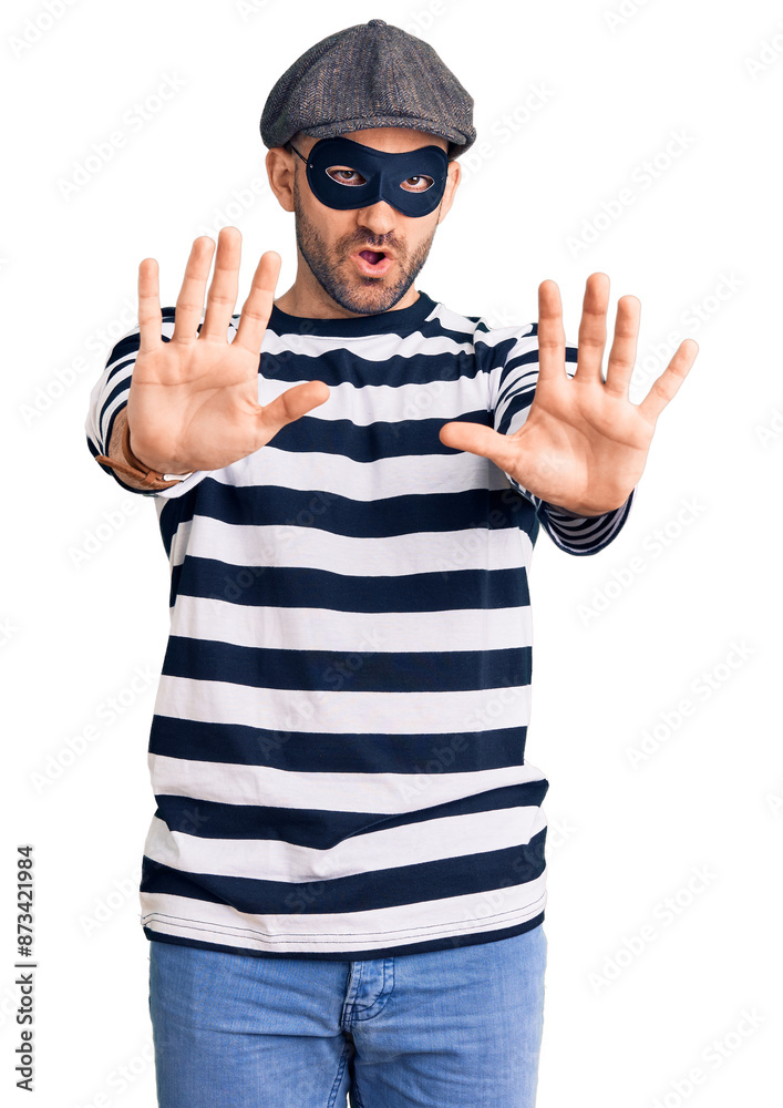 Young handsome man wearing burglar mask doing stop gesture with hands palms, angry and frustration expression Young handsome man wearing burglar mask doing stop gesture with hands palms, angry and frustration expression
