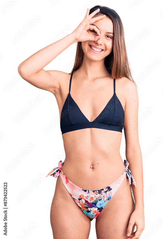 Fototapeta premium Young beautiful girl wearing bikini smiling happy doing ok sign with hand on eye looking through fingers