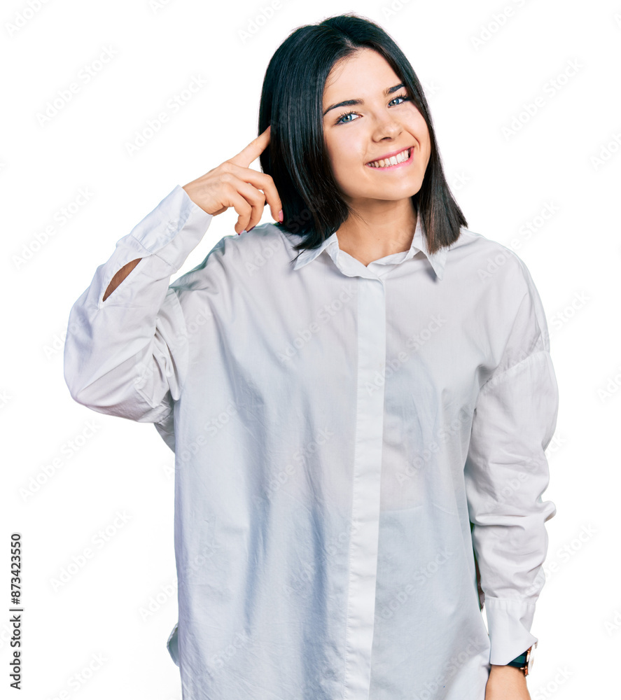 Young brunette woman with blue eyes wearing oversize white shirt smiling pointing to head with one finger, great idea or thought, good memory Young brunette woman with blue eyes wearing oversize white shirt smiling pointing to head with one finger, great idea or thought, good memory