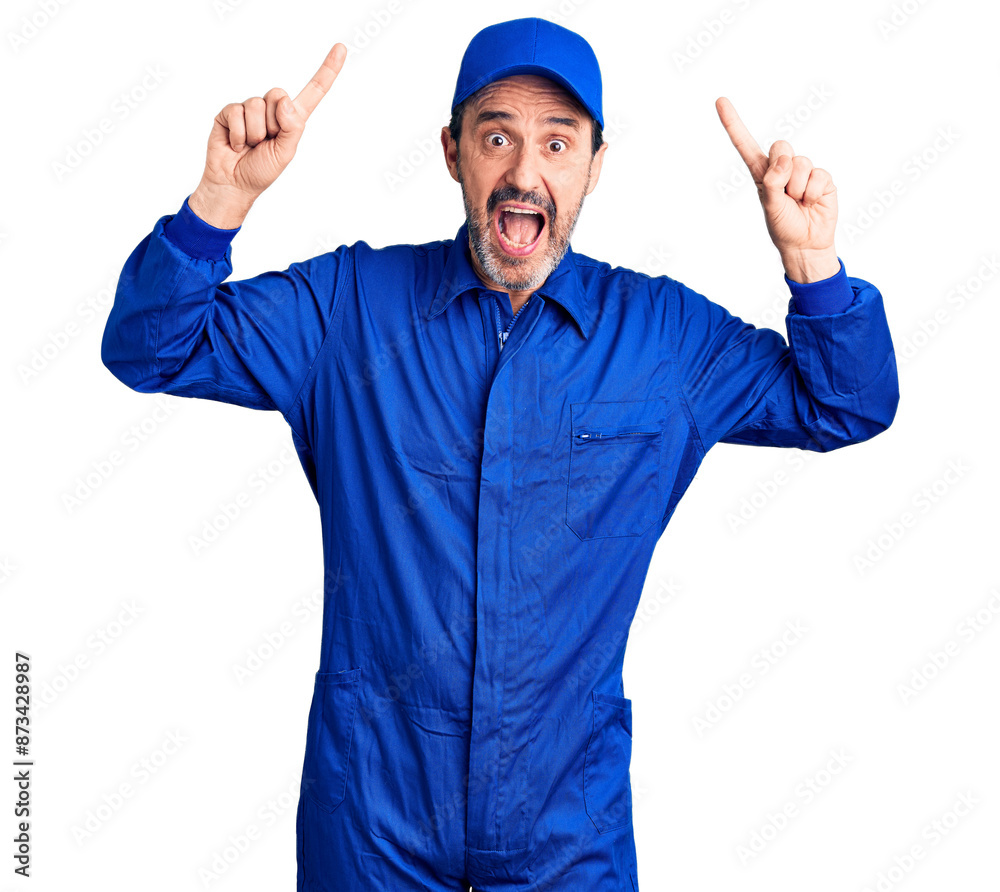Middle age handsome man wearing mechanic uniform smiling amazed and surprised and pointing up with fingers and raised arms. Middle age handsome man wearing mechanic uniform smiling amazed and surprised and pointing up with fingers and raised arms.