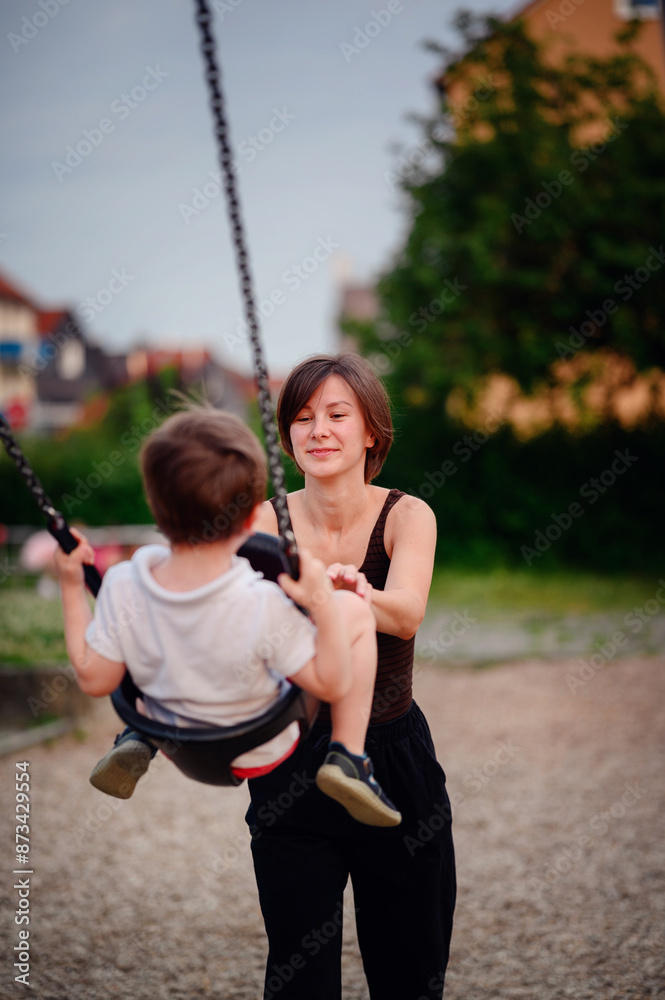 A mother pushing her laughing young son on a swing at the playground, capturing a moment of pure joy and playful bonding together outdoors. A mother pushing her laughing young son on a swing at the playground, capturing a moment of pure joy and playful bonding together outdoors.