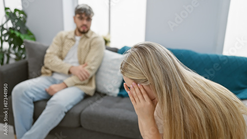 A distressed woman crying in the foreground with a concerned man sitting on a couch in a modern living room. photo