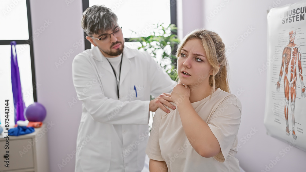 A man physiotherapist assesses the shoulder pain of a young woman patient in a well-equipped rehabilitation clinic. A man physiotherapist assesses the shoulder pain of a young woman patient in a well-equipped rehabilitation clinic.