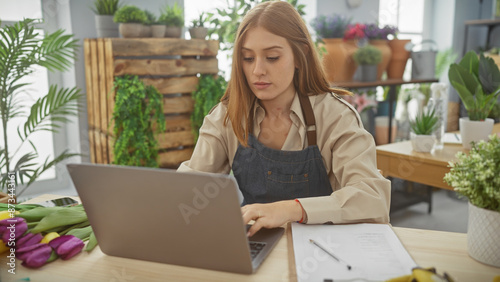 Focused woman with laptop in a flower shop surrounded by plants, embodying entrepreneurship and small business. © Krakenimages.com