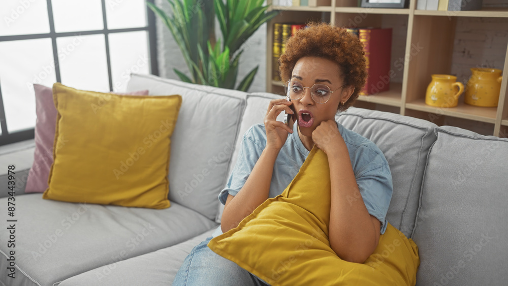 A surprised african woman reacts while talking on the phone, sitting in a modern living room with vibrant decor. A surprised african woman reacts while talking on the phone, sitting in a modern living room with vibrant decor.