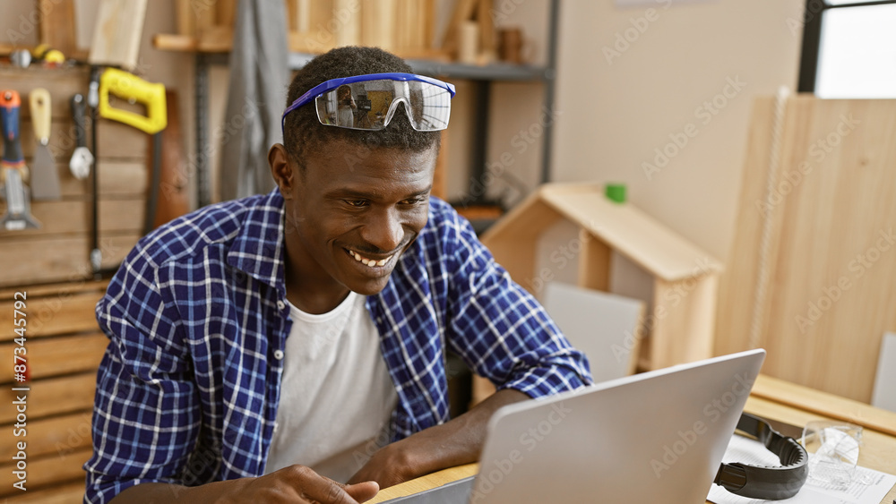 Smiling african man using laptop in a woodworking workshop. Smiling african man using laptop in a woodworking workshop.