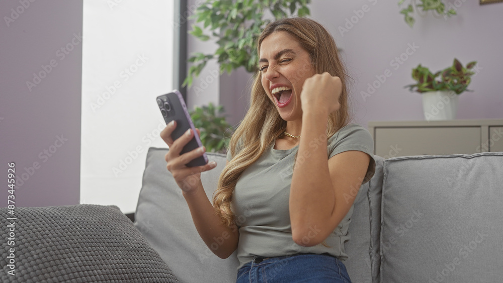Cheerful young woman reacting excitedly to content on her smartphone in a modern living room Cheerful young woman reacting excitedly to content on her smartphone in a modern living room