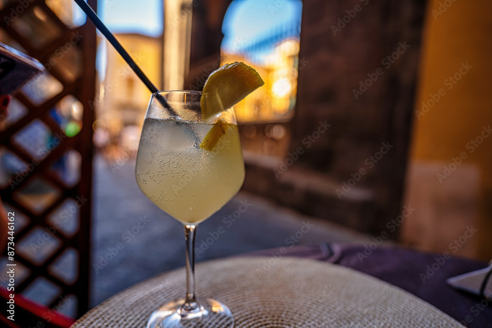 Summer limoncello tonic cocktail on a table of a restaurant with tables kept outdoors on a street, it contains soda, prosecco wine and limoncella alcohol