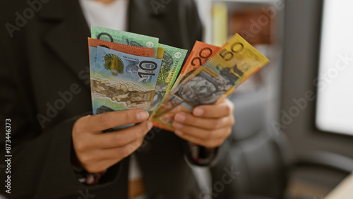 A professional woman holds australian currency in a modern office, depicting finance and workplace themes.