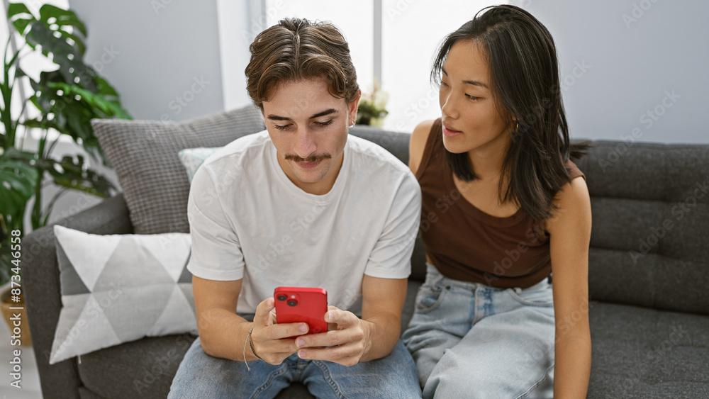 A young interracial couple engages with a smartphone in the cozy living room of their modern home. A young interracial couple engages with a smartphone in the cozy living room of their modern home.