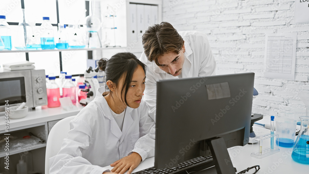 Man and woman scientists in laboratory analyzing data on computer amidst equipment. Man and woman scientists in laboratory analyzing data on computer amidst equipment.