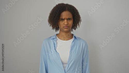 Young african american woman with curly hair in a blue shirt standing against an isolated white background.