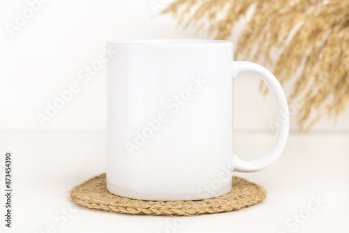 Mockup of white mug on table with jute coaster and dried flowers. Blank 11 oz ceramic coffee cup mock up in Boho style, neutral color.