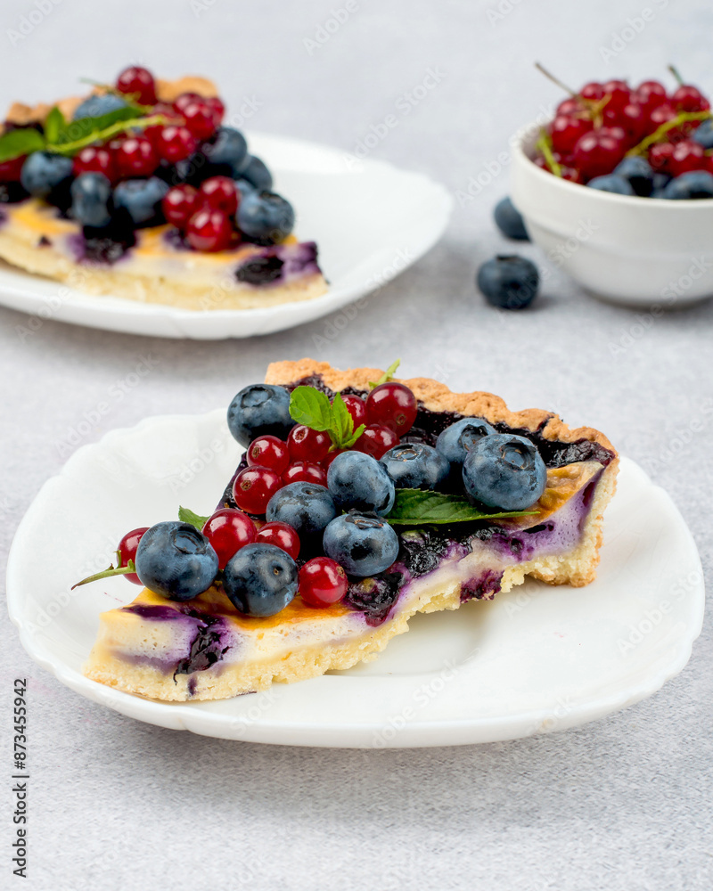 Two pieces of shortbread cake with blueberries and red currants, garnished with a mint leaf. Seasonal, bright, summer baked goods. Two pieces of shortbread cake with blueberries and red currants, garnished with a mint leaf. Seasonal, bright, summer baked goods.