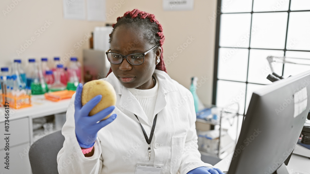 African woman scientist examining a potato in a laboratory with computers, colorful reagents, and medical equipment. African woman scientist examining a potato in a laboratory with computers, colorful reagents, and medical equipment.