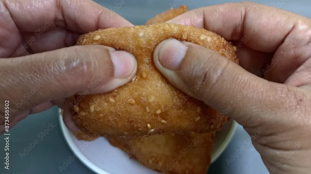Hand is breaking Bolang baling or Odading into two. fried bread in cubes or blocks, with a light brown crunchy outer skin and sprinkled with sesame seeds, the inside is empty and fluffy. Hand is breaking Bolang baling or Odading into two. fried bread in cubes or blocks, with a light brown crunchy outer skin and sprinkled with sesame seeds, the inside is empty and fluffy.