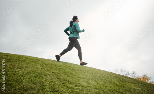 Music, running and woman on grass at hill for fitness, jog or healthy body in winter on mockup space. Earphones, cardio or person exercise for sport, wellness or training to workout in nature at park © peopleimages.com