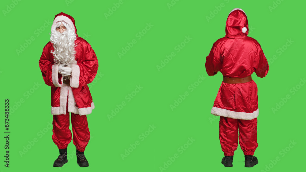 Fototapeta premium Santa claus on full body greenscreen backdrop, joyful person trying to spread christmas spirit with traditional festive costume. Saint nick with hat and beard, winter holiday celebration.