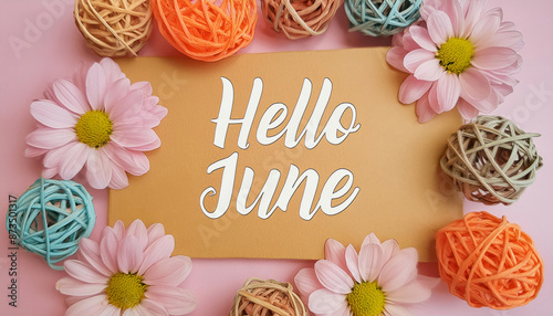 Hello June calligraphic text message written on recycled paper label tag on pink decorative floral background with reused material flowers and balls in peach, beige and turquoise colors. 
