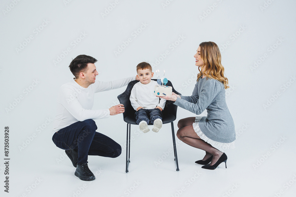 Fototapeta premium A happy married couple with a small son and a delicious cake in their hands. Mom dad and smiling son celebrating birthday. Stylish family.