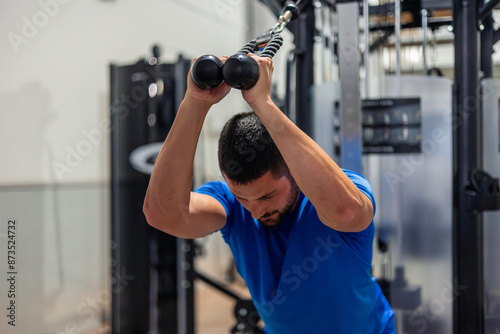 Foto young athlete does triceps exercise with high pulley machine in gym during stren