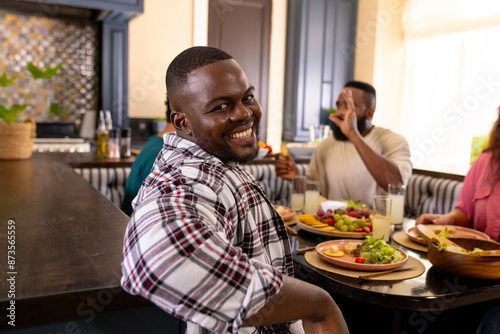 Smiling man enjoying meal with diverse friends at dining table, sharing laughter and food