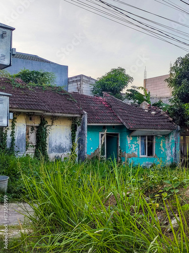 abandoned subsidized house in disrepair, overgrown with wild vines and nearly collapsing, located in a simple housing complex in Southeast Asia, Indonesia