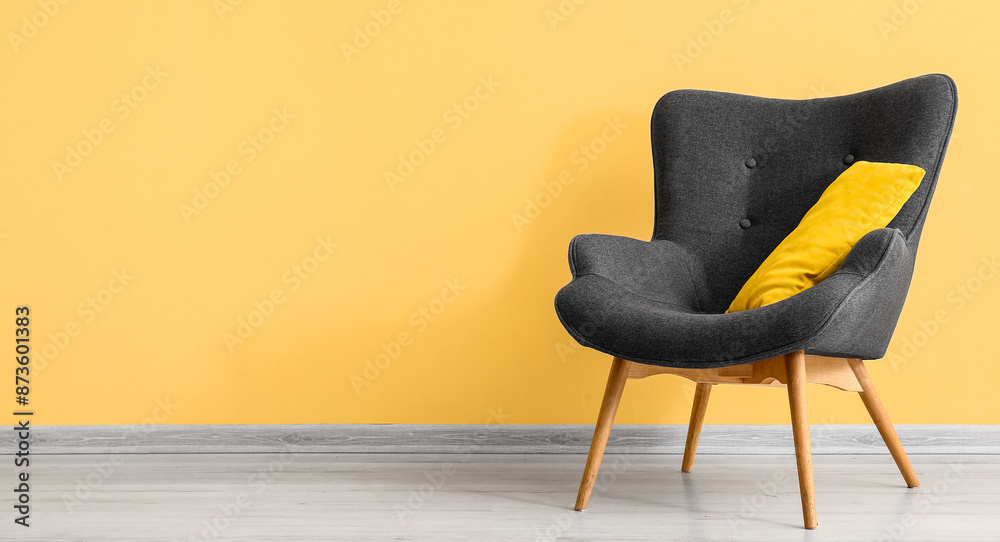 Stylish grey armchair with cushion near yellow wall Stylish grey armchair with cushion near yellow wall