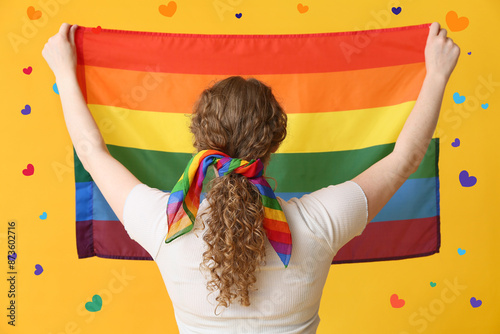 Young woman with LGBT flag and hairscarf on yellow background, back view photo