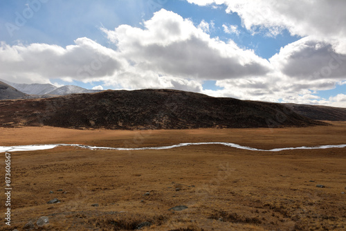 The yellowed flat steppe crosses the winding bed of a beautiful river flowing along the mountain range on an autumn cloudy day.