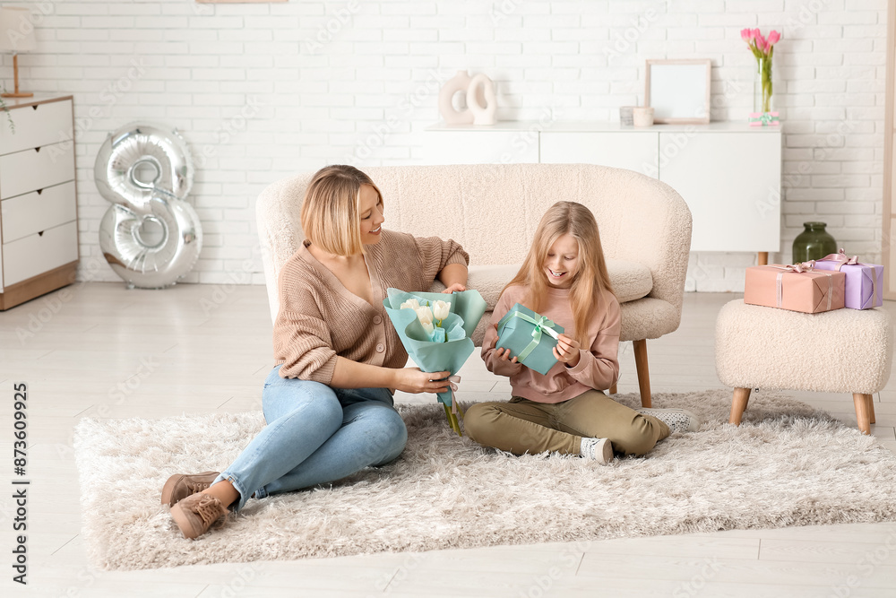 Beautiful young woman holding bouquet of tulips and her cute little daughter with gift box sitting on carpet in living room Beautiful young woman holding bouquet of tulips and her cute little daughter with gift box sitting on carpet in living room