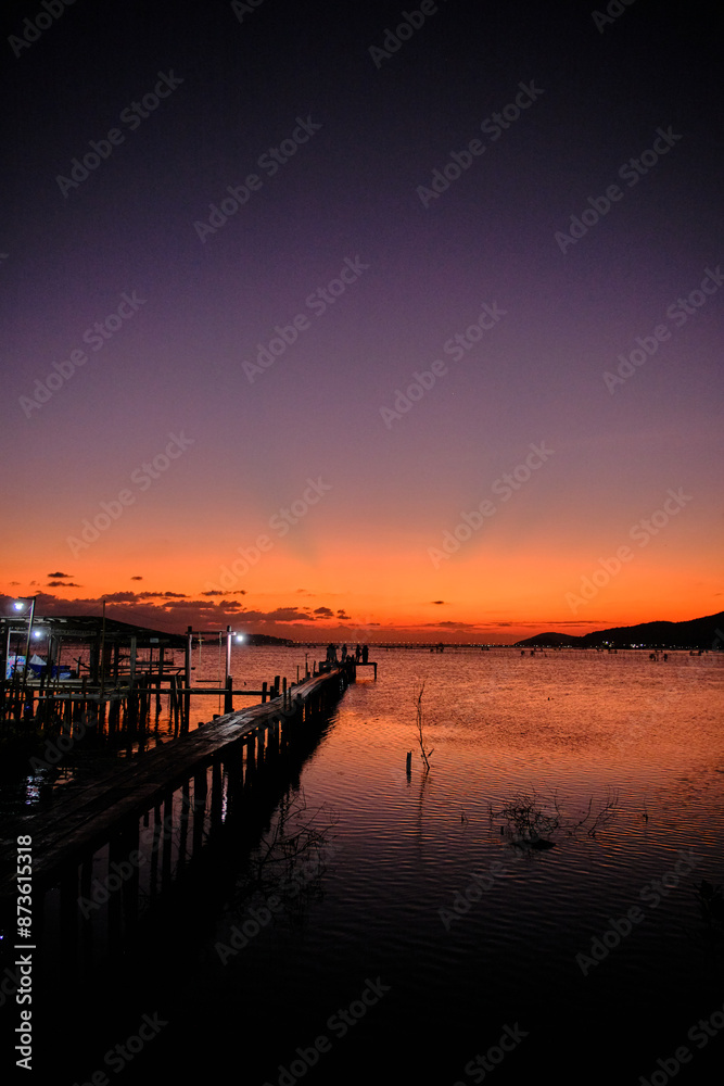 Obraz premium Golden hues of sunset paint the sky and reflect on the tranquil waters, creating a serene and picturesque scene by the pier