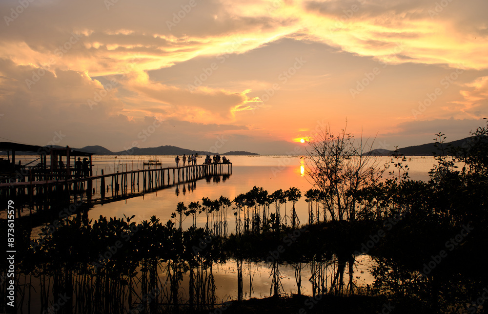 Obraz premium Golden hues of sunset paint the sky and reflect on the tranquil waters, creating a serene and picturesque scene by the pier