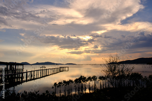 Golden hues of sunset paint the sky and reflect on the tranquil waters, creating a serene and picturesque scene by the pier