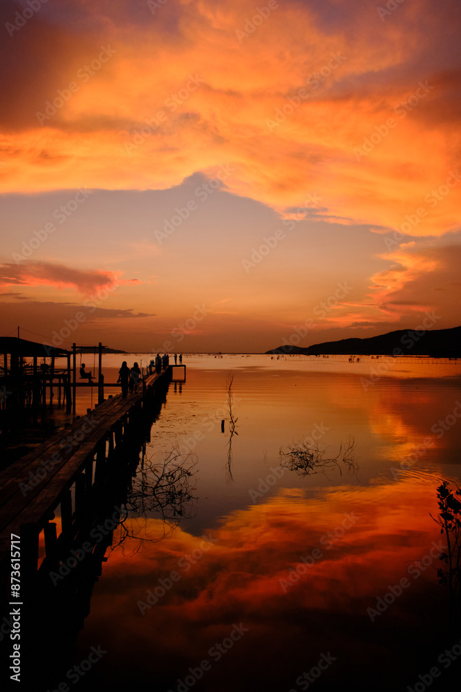 Obraz premium Golden hues of sunset paint the sky and reflect on the tranquil waters, creating a serene and picturesque scene by the pier