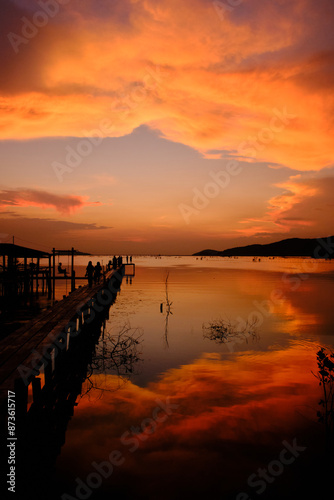 Golden hues of sunset paint the sky and reflect on the tranquil waters, creating a serene and picturesque scene by the pier