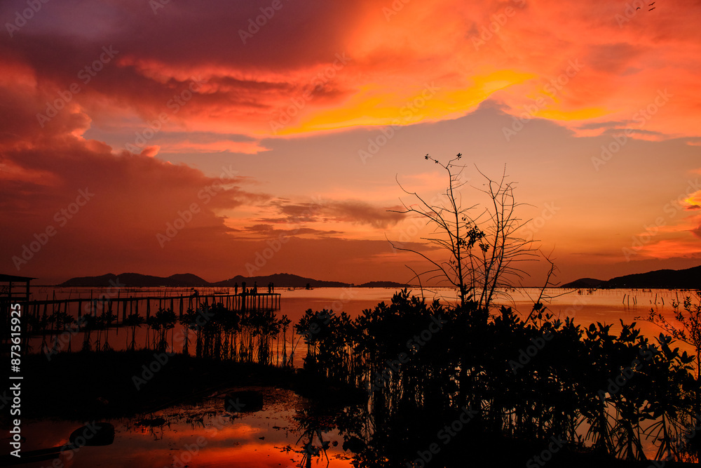 Obraz premium Golden hues of sunset paint the sky and reflect on the tranquil waters, creating a serene and picturesque scene by the pier