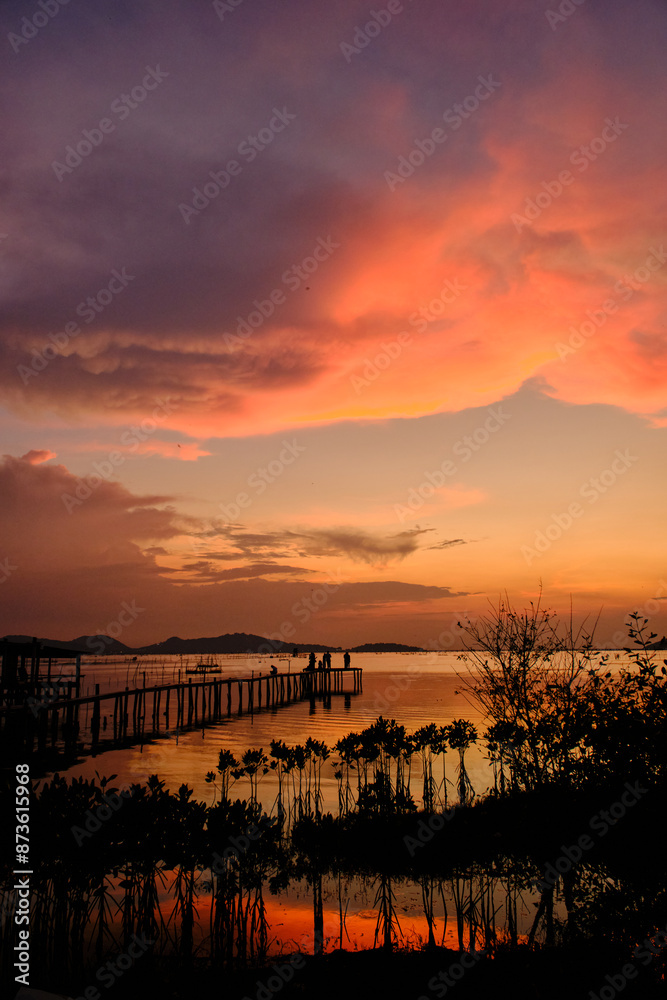 Obraz premium Golden hues of sunset paint the sky and reflect on the tranquil waters, creating a serene and picturesque scene by the pier