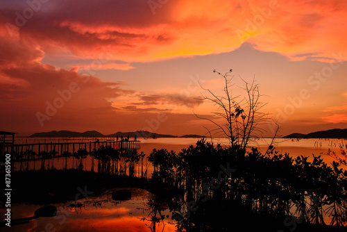 Golden hues of sunset paint the sky and reflect on the tranquil waters, creating a serene and picturesque scene by the pier