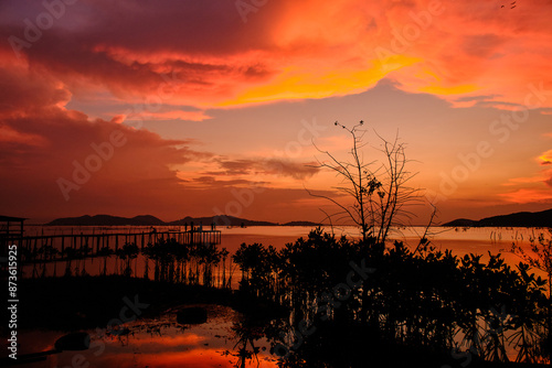 Golden hues of sunset paint the sky and reflect on the tranquil waters, creating a serene and picturesque scene by the pier