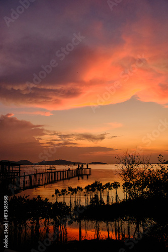 Golden hues of sunset paint the sky and reflect on the tranquil waters, creating a serene and picturesque scene by the pier