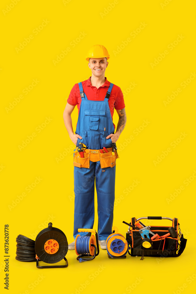 Obraz premium Young male electrician with tool bag and extension cable reels on yellow background