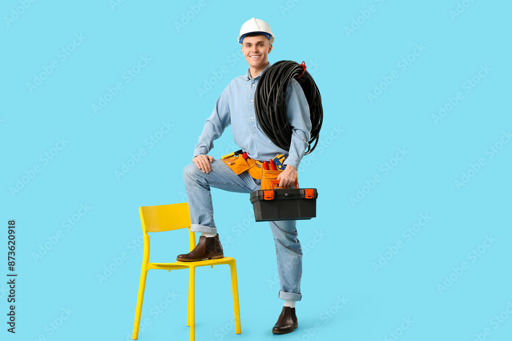 Young male electrician with tool box and flexible conduit tube on blue background Young male electrician with tool box and flexible conduit tube on blue background