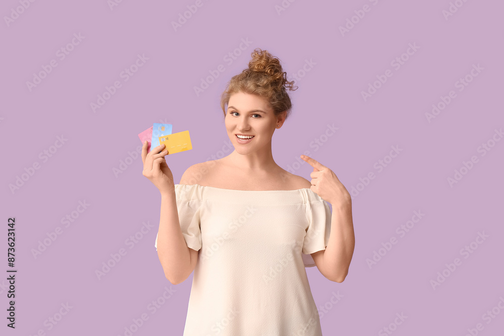 Beautiful young woman pointing at credit cards on purple background Beautiful young woman pointing at credit cards on purple background