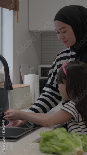 Asian Muslim Mother Teaching Daughter Washing Fresh Fruit or Preparing Food In Kitchen At Home